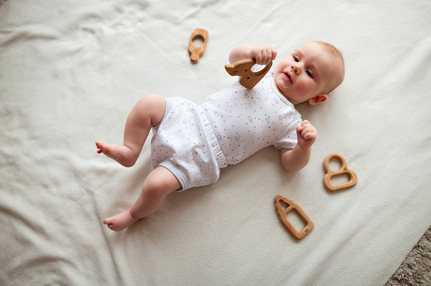 Baby lying on a white blanket with wooden toys around